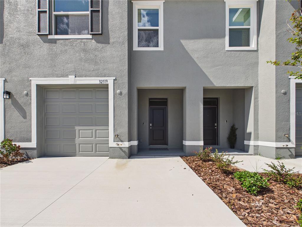 A gray two-story townhouse features a single-car garage and two recessed front entry doors — 32519 WELLING BLADE LOOP, WESLEY CHAPEL, FL