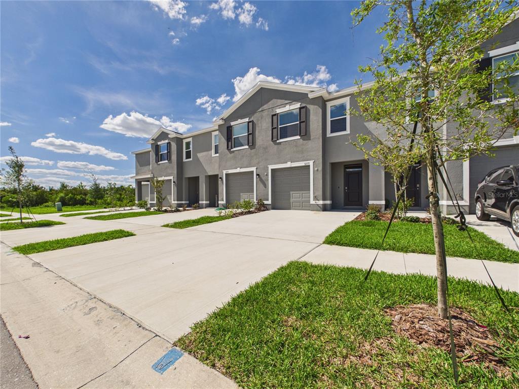 A row of gray two-story townhomes with attached garages and concrete driveways under a blue sky — 32519 WELLING BLADE LOOP, WESLEY CHAPEL, FL