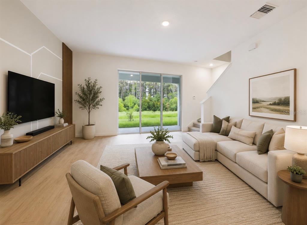 A modern living room features a sectional sofa, wood media console, and sliding glass doors — 32519 WELLING BLADE LOOP, WESLEY CHAPEL, FL