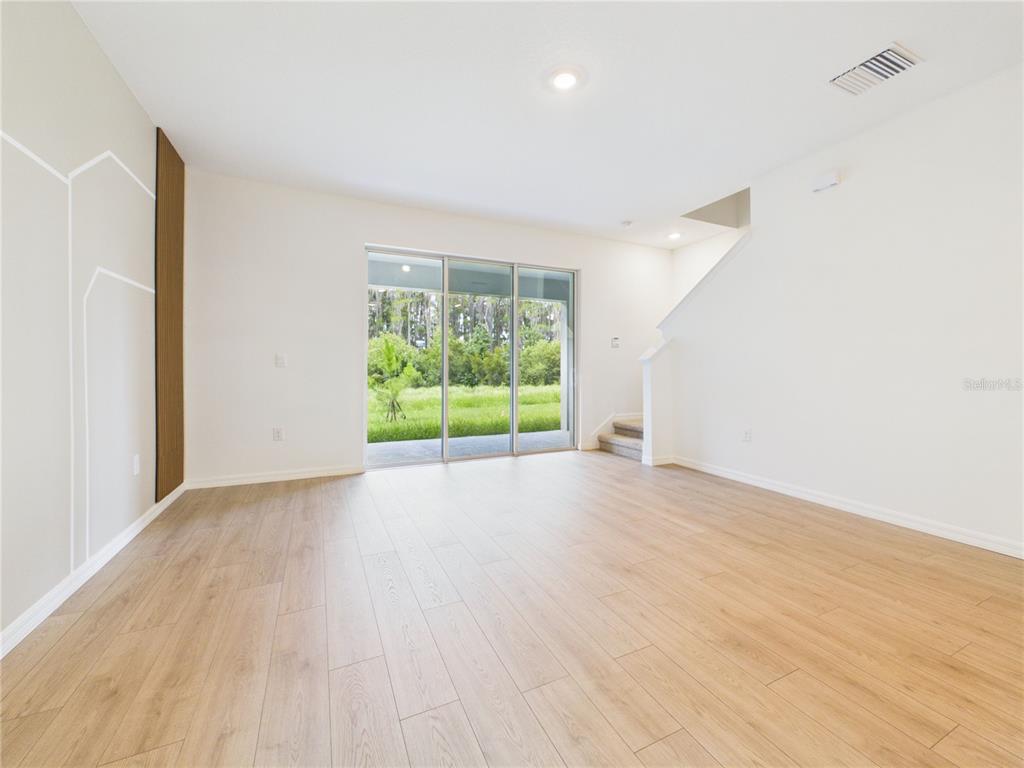 An empty living room features light wood-look flooring, white walls, and sliding glass patio doors — 32519 WELLING BLADE LOOP, WESLEY CHAPEL, FL