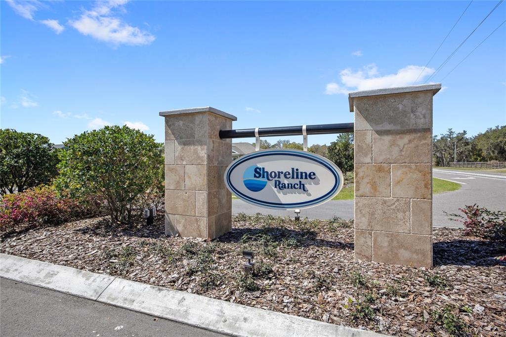 A stone monument sign for Shoreline Ranch stands beside a paved road under a blue sky — 38514 WOODED MEADOW DRIVE, UMATILLA, FL