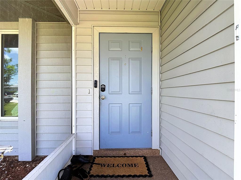 A light blue front door with a welcome mat sits on a covered porch — 1832 VAN LOON TERRACE, CAPE CORAL, FL