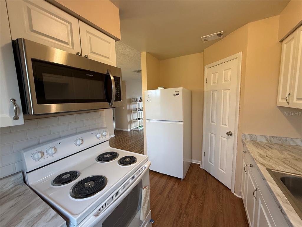 A kitchen features white cabinets, stainless steel appliances, a white stove, and wood-look flooring — 1920 E EDGEWOOD DRIVE UNIT N8, LAKELAND, FL