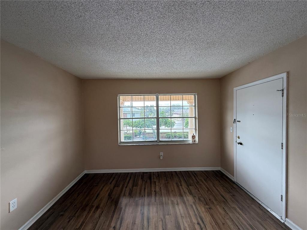 An empty room features light-colored walls, a popcorn ceiling, wood-look flooring, and a large window — 1920 E EDGEWOOD DRIVE UNIT N8, LAKELAND, FL