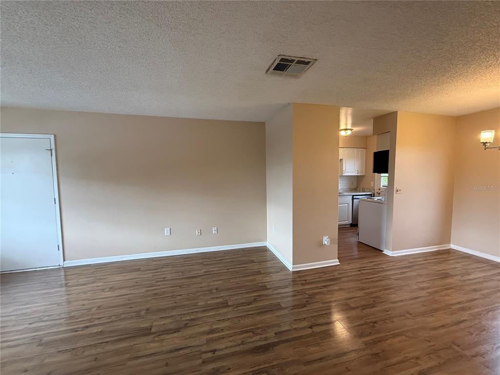 An open living area with wood-look flooring leads to a kitchen with white cabinets — 1920 E EDGEWOOD DRIVE UNIT N8, LAKELAND, FL
