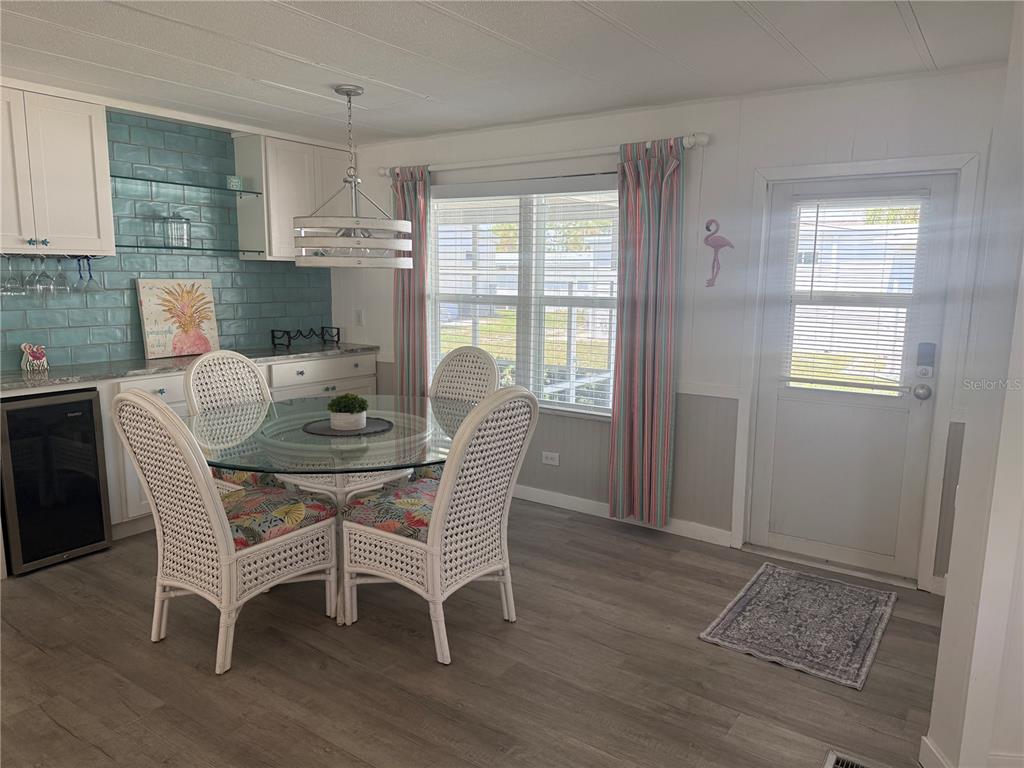 A dining area features a glass-topped table, white wicker chairs, blue tile backsplash, and wood-look flooring — 5710 ORANGE BLOSSOM ROAD, VENICE, FL