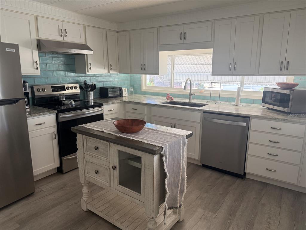 A kitchen features white cabinets, a teal subway tile backsplash, stainless steel appliances, and an island — 5710 ORANGE BLOSSOM ROAD, VENICE, FL