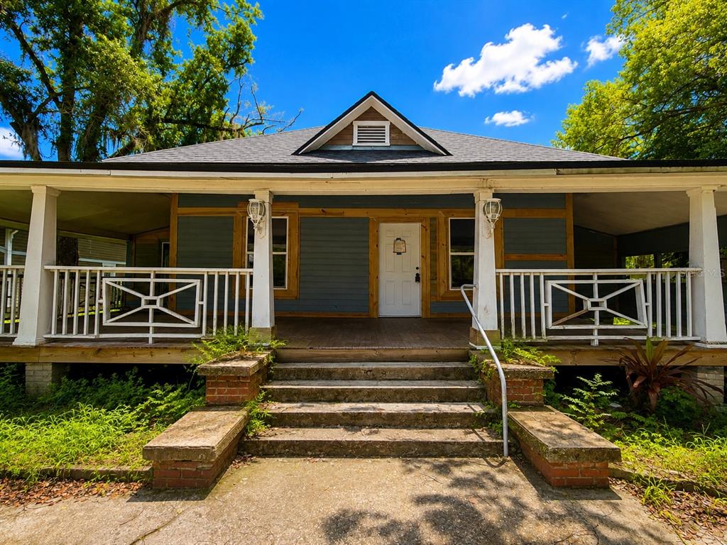 A blue house with a wrap-around porch, white railings, and concrete steps leading to the entrance — 204 N MONROE AVENUE, ARCADIA, FL