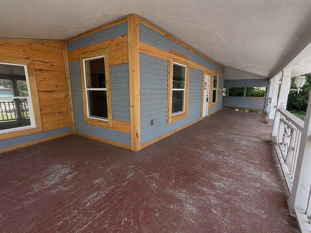 A wide, covered porch features weathered red decking, blue siding, and natural wood trim — 204 N MONROE AVENUE, ARCADIA, FL