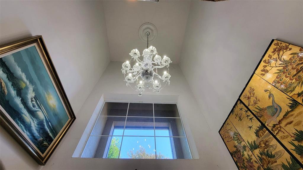 A chandelier hangs in a high-ceilinged room with a large window and wall art — 3731 EAGLE ISLE CIRCLE, KISSIMMEE, FL
