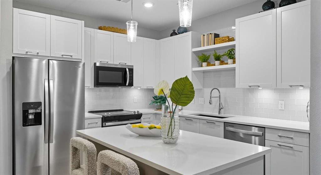 A modern kitchen features white cabinetry, stainless steel appliances, a quartz island, and subway tile — 32475 SUGARPLUM LOOP UNIT 4120, WESLEY CHAPEL, FL