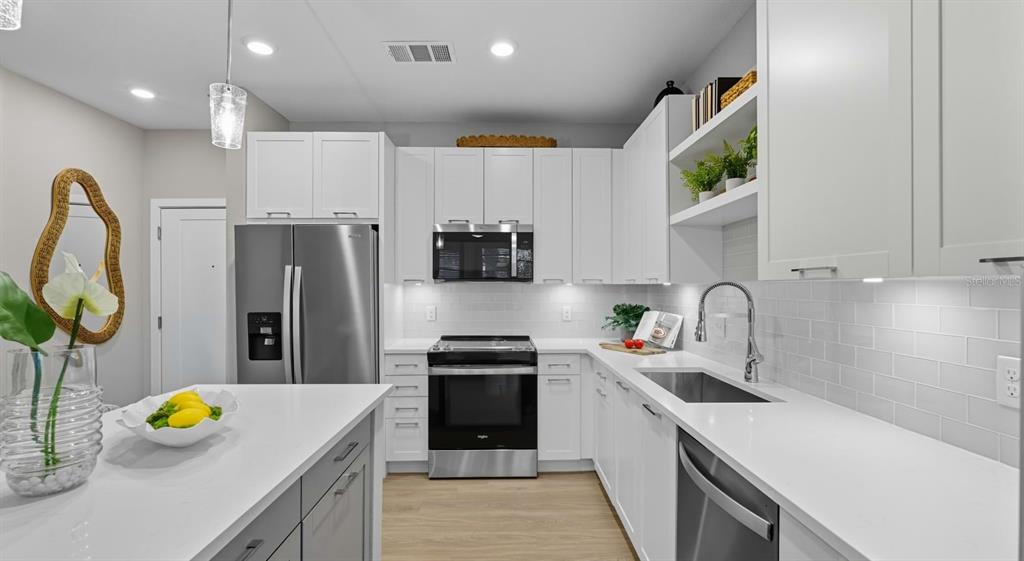A modern kitchen features white cabinets, stainless steel appliances, a white island, and subway tile backsplash — 32475 SUGARPLUM LOOP UNIT 4120, WESLEY CHAPEL, FL