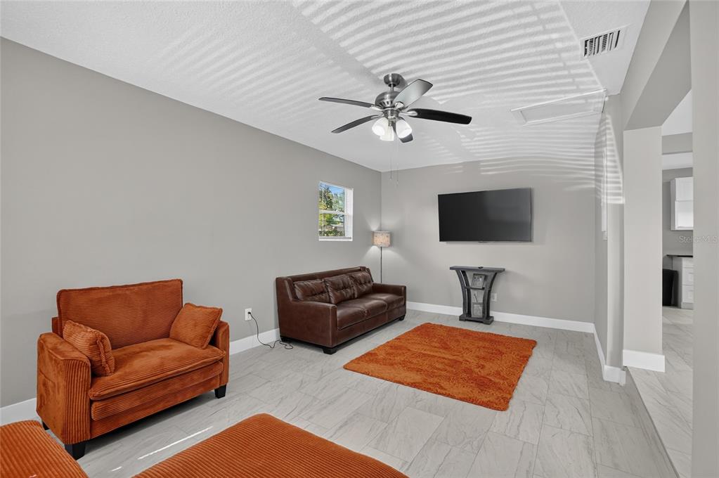 A living room features gray walls, tile flooring, a ceiling fan, and orange furniture — 10420 N 22ND STREET, TAMPA, FL
