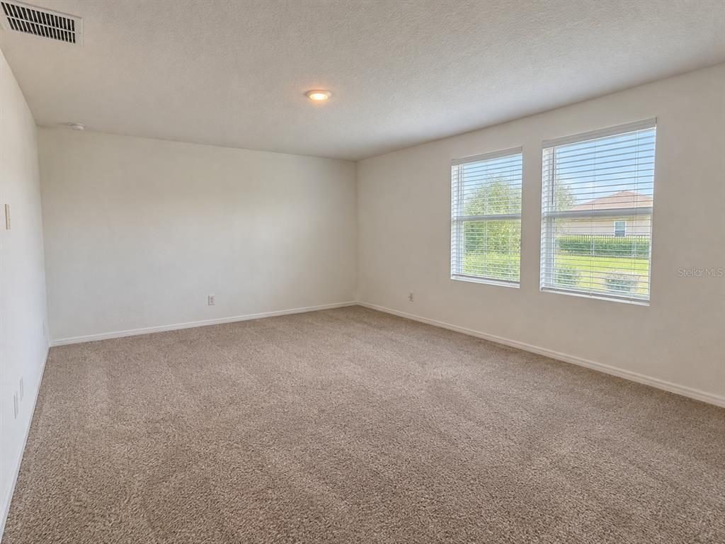 An empty bedroom features beige carpeting, white walls, and a large floral accent wall — 2074 DERWENT DRIVE, DAVENPORT, FL