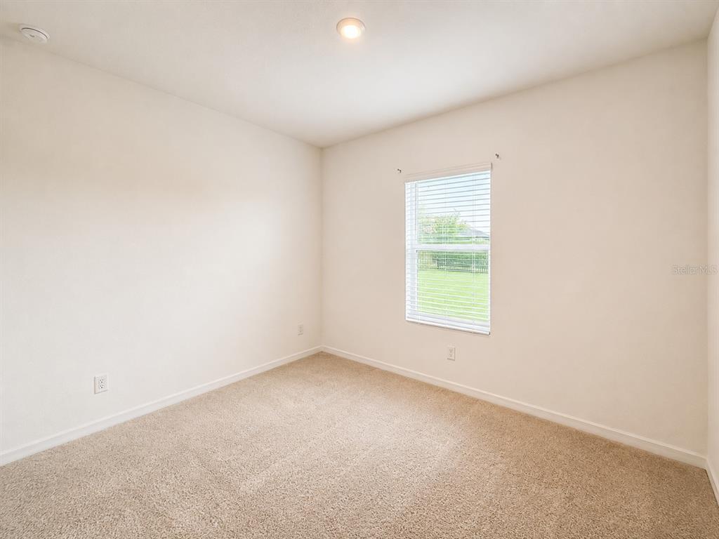 An empty bedroom features beige carpet, off-white walls, a single window, and a ceiling light — 2074 DERWENT DRIVE, DAVENPORT, FL