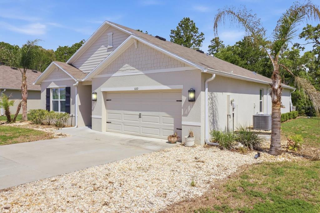 A single-story house with a beige stucco exterior, a two-car garage, and a gravel yard — 660 HICKORY COURSE LOOP, OCALA, FL