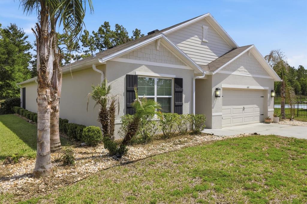 A single-story house with a beige stucco exterior, dark shutters, and a two-car garage — 660 HICKORY COURSE LOOP, OCALA, FL