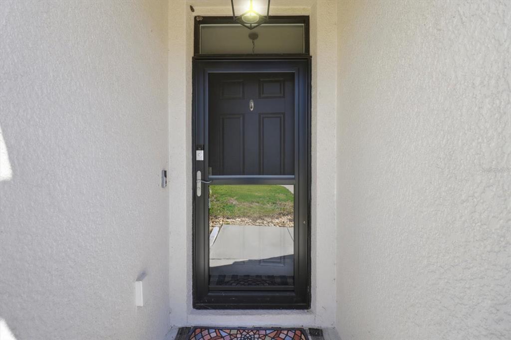 A black storm door with a glass panel is set within a white stucco entryway — 660 HICKORY COURSE LOOP, OCALA, FL