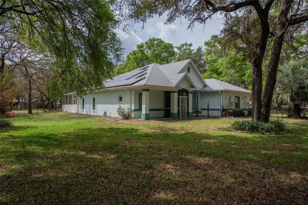 A single-story house with a light-colored exterior, solar panels on the roof, and surrounding trees — 1210 E ORIOLE COURT, HERNANDO, FL