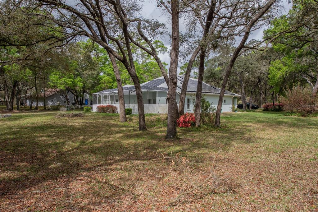 A house with a screened-in pool enclosure and solar panels sits among mature trees — 1210 E ORIOLE COURT, HERNANDO, FL