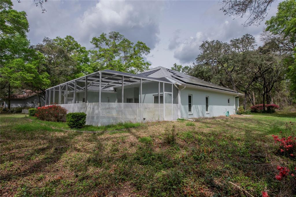 A light-colored house with a screened-in pool enclosure sits on a wooded, grassy lot — 1210 E ORIOLE COURT, HERNANDO, FL