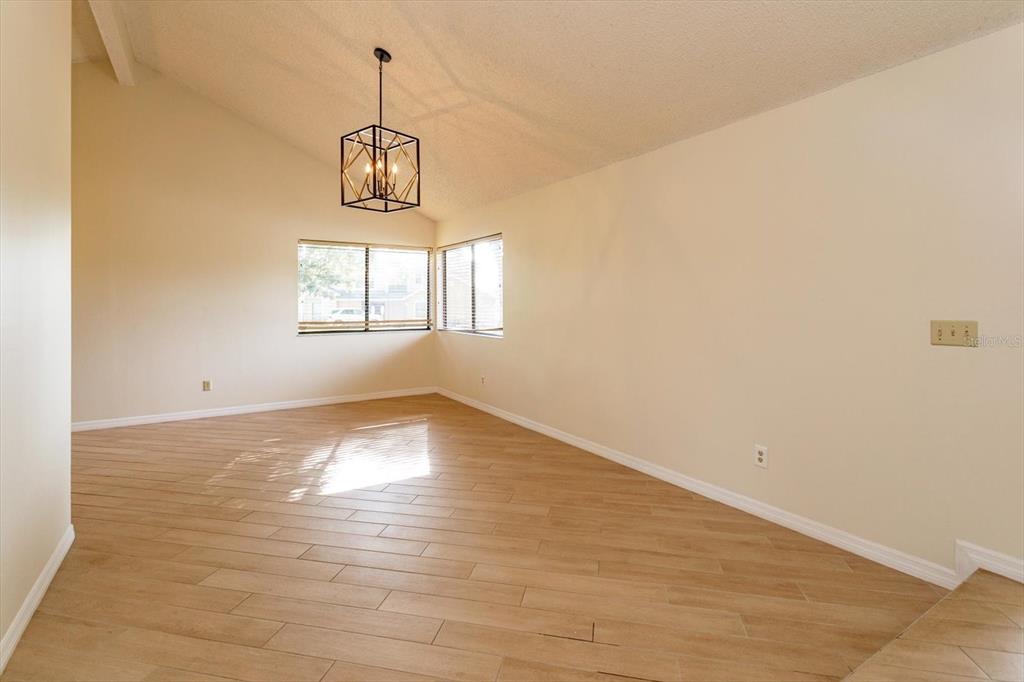An empty room with light wood-look tile flooring, a vaulted ceiling, and a geometric chandelier — 7925 SNOWBERRY CIRCLE, ORLANDO, FL