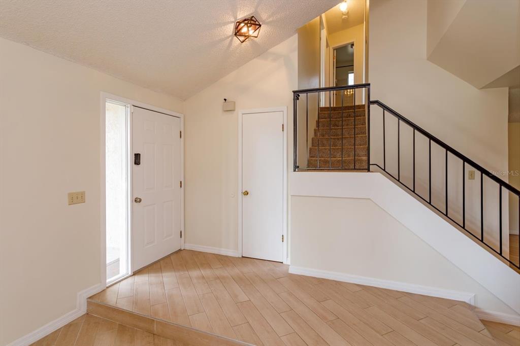 An entryway features light wood-look tile flooring, a white front door, and a carpeted staircase — 7925 SNOWBERRY CIRCLE, ORLANDO, FL