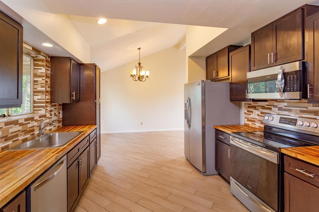 A kitchen with dark wood cabinets, butcher block countertops, and stainless steel appliances — 7925 SNOWBERRY CIRCLE, ORLANDO, FL