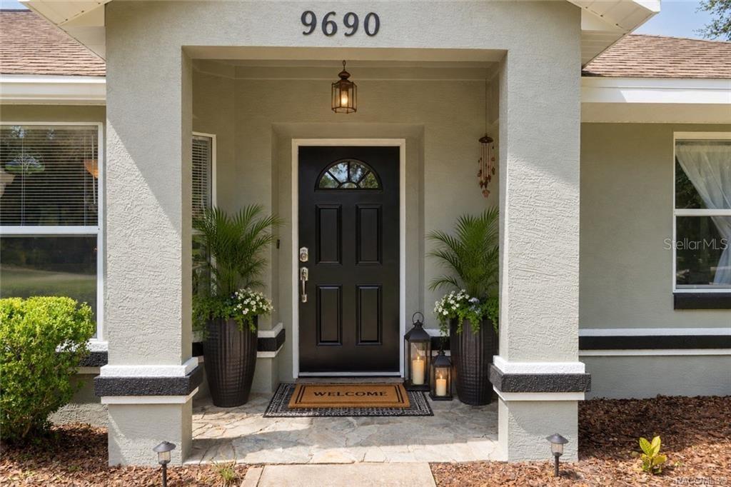 A front entryway with a black door, stone porch, and two large potted plants — 9690 N ALDER AVENUE, CRYSTAL RIVER, FL