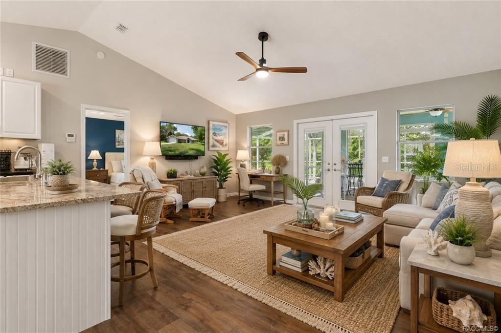 A bright living room features a vaulted ceiling, wood-look flooring, and a large area rug — 9690 N ALDER AVENUE, CRYSTAL RIVER, FL
