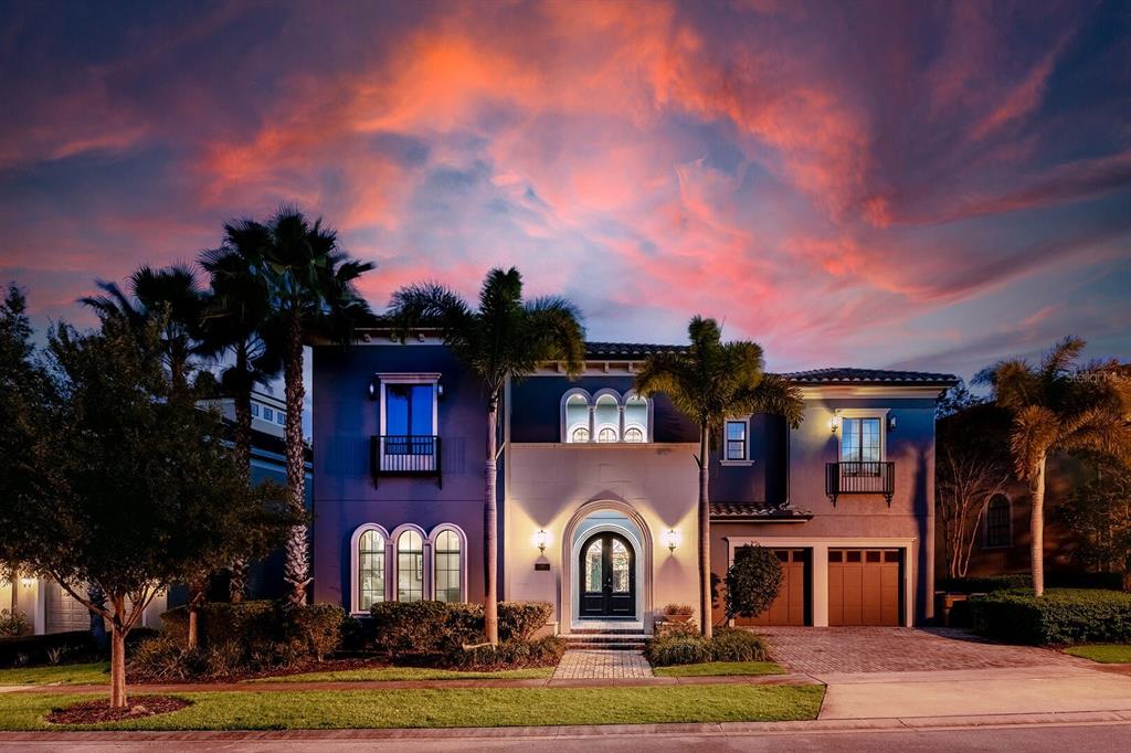 A two-story house with a blue and white exterior, arched entryway, and palm trees at sunset — 445 MUIRFIELD LOOP, REUNION, FL