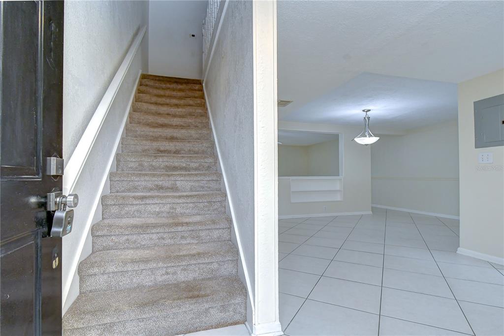 A carpeted staircase leads upward next to a tiled room with a hanging light fixture — 230 CYPRESS PLACE, OLDSMAR, FL
