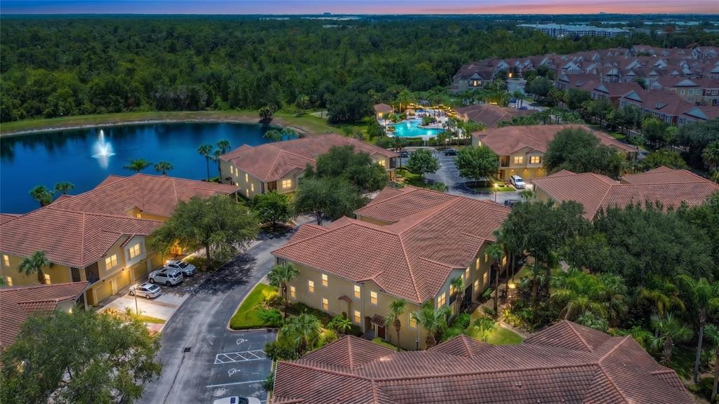 An aerial view shows multi-story apartment buildings with tile roofs surrounding a pond and pool — 2742 OAKWATER DRIVE UNIT 104, KISSIMMEE, FL