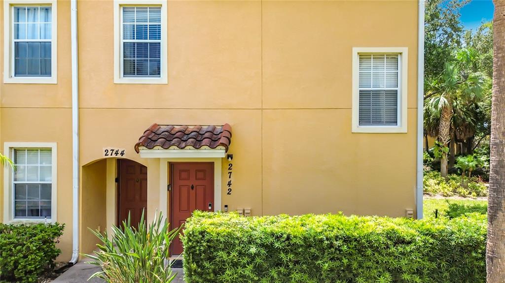 A two-story yellow stucco townhouse exterior features a red front door and a small hedge — 2742 OAKWATER DRIVE UNIT 104, KISSIMMEE, FL