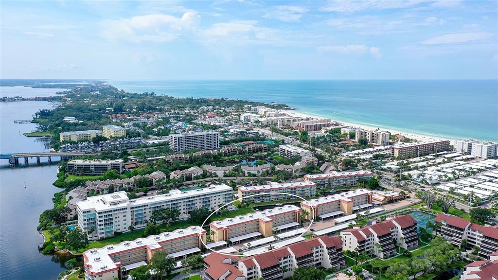 An aerial view shows a multi-story apartment complex near a coastal waterway and beach — 1300 N PORTOFINO DRIVE UNIT 103, SARASOTA, FL