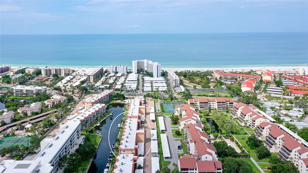 An aerial view shows a multi-story residential complex with a canal and nearby beach — 1300 N PORTOFINO DRIVE UNIT 103, SARASOTA, FL