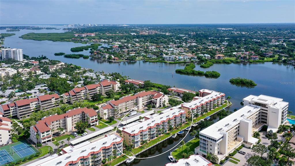 An aerial view shows multi-story apartment buildings situated along a canal near a large bay — 1300 N PORTOFINO DRIVE UNIT 103, SARASOTA, FL