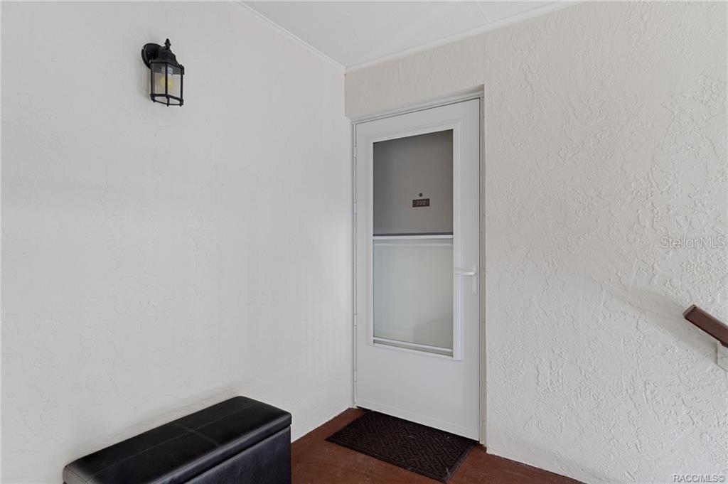 A white exterior door with a glass panel is set into a textured white wall — 2400 FOREST DRIVE UNIT 222, INVERNESS, FL