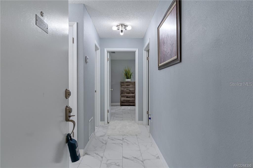 A hallway with white marble-look tile flooring leads to a doorway with a wooden dresser — 2400 FOREST DRIVE UNIT 222, INVERNESS, FL