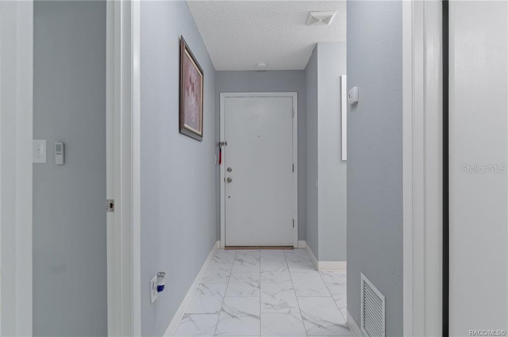 A hallway with light gray walls, white trim, and white marble-look tile flooring — 2400 FOREST DRIVE UNIT 222, INVERNESS, FL