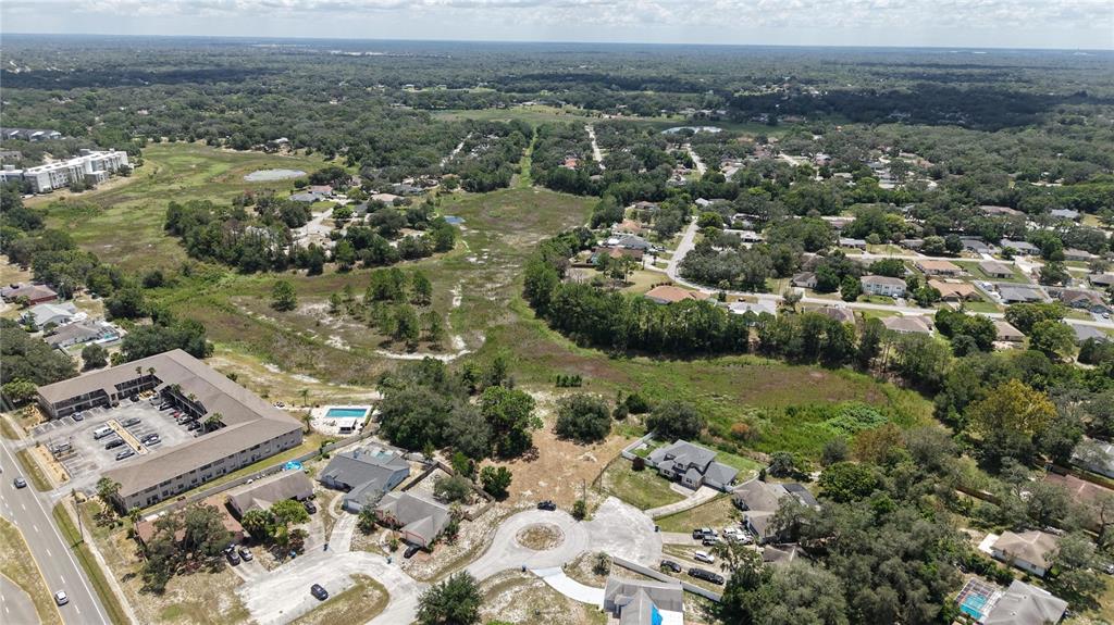 An aerial view shows a suburban neighborhood with houses, a large apartment complex, and undeveloped land — 1170 PORT COURT, SPRING HILL, FL
