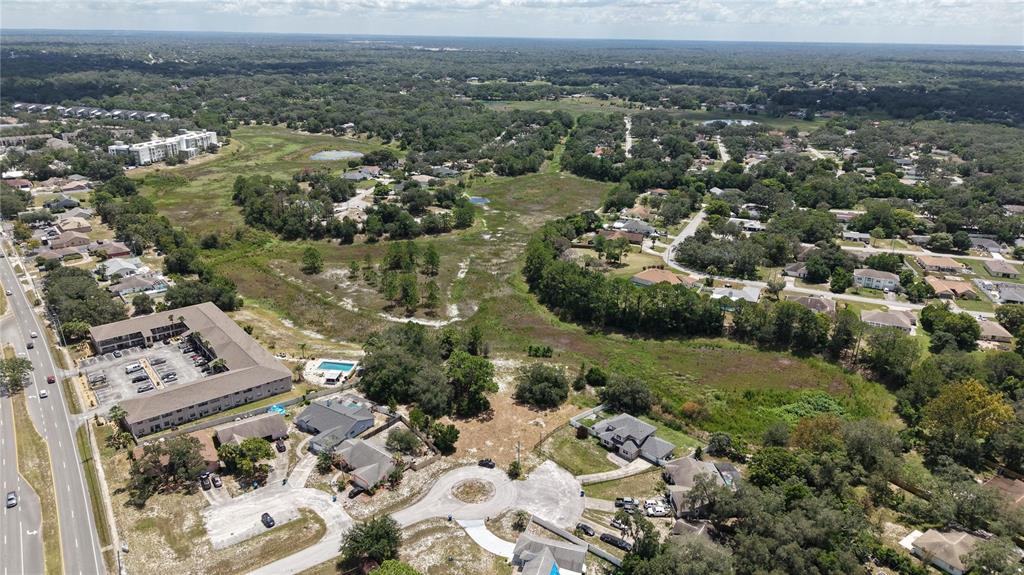 An aerial view shows a suburban neighborhood with houses, a multi-story apartment complex, and undeveloped land — 1170 PORT COURT, SPRING HILL, FL