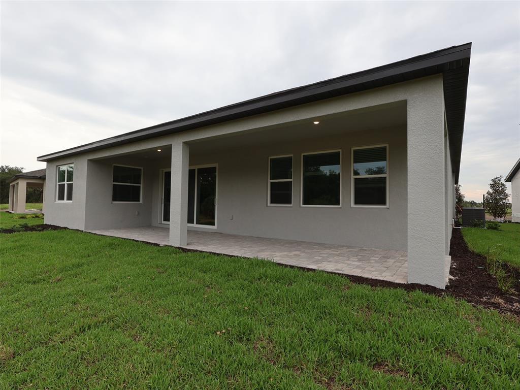 A gray stucco house features a covered back patio with pavers and a grassy yard — 3689 142ND TERRACE E, PARRISH, FL