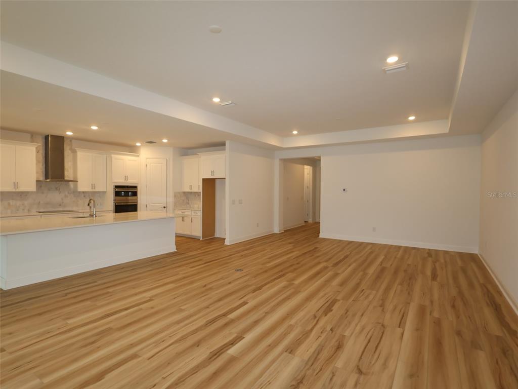 An open-concept kitchen and living area featuring white cabinetry, a large island, and wood-look flooring — 3689 142ND TERRACE E, PARRISH, FL