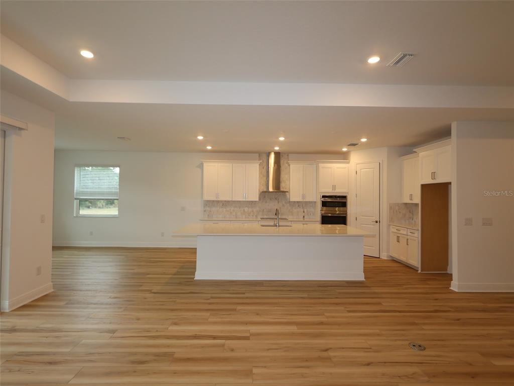 A modern kitchen features white cabinetry, a large central island, and light wood flooring — 3689 142ND TERRACE E, PARRISH, FL