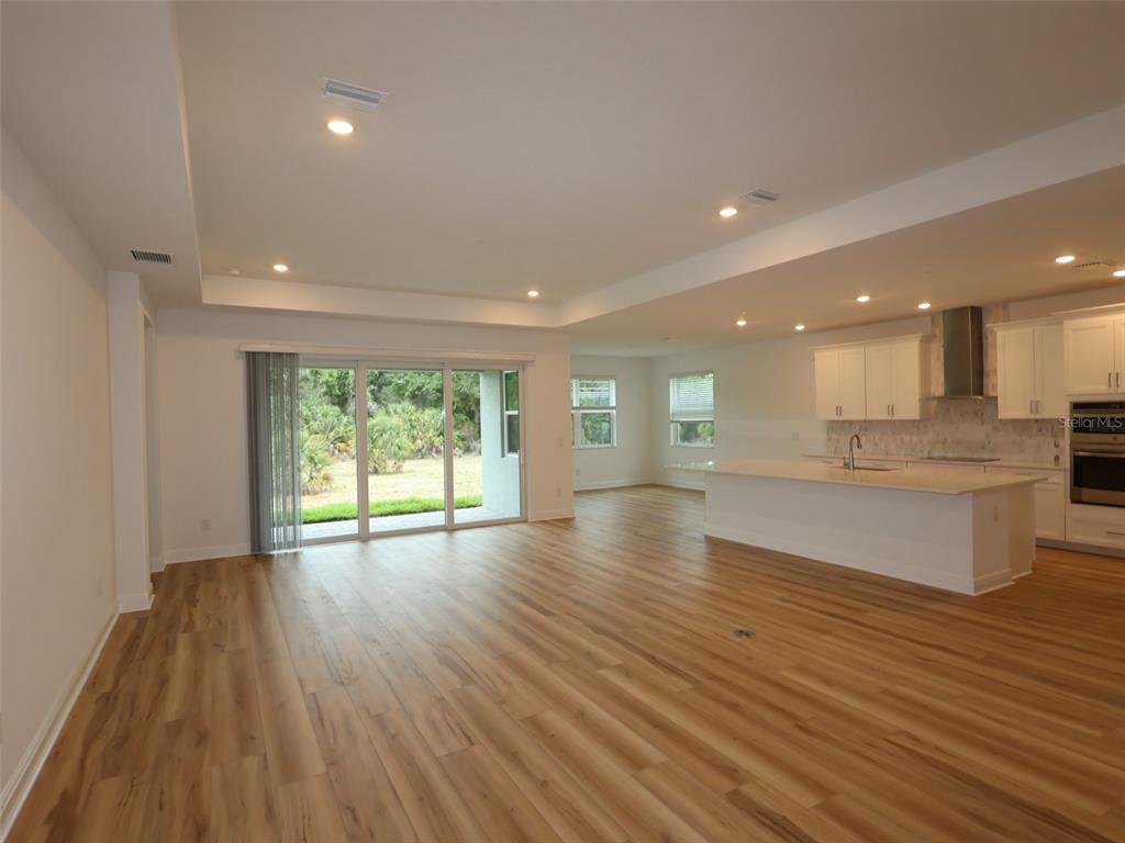 An open-concept living area features light wood-look flooring, a kitchen island, and sliding glass doors — 3689 142ND TERRACE E, PARRISH, FL