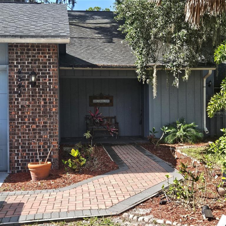 A brick-sided house features a gray-painted recessed entryway with a bench and a brick walkway — 4841 HAWKSHEAD PARK, SARASOTA, FL