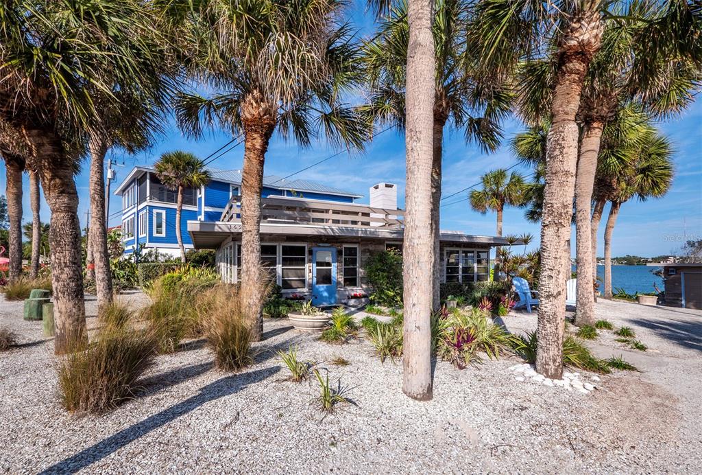 A single-story house with a flat roof and blue door sits among palm trees near water — 1620 CASEY KEY ROAD, NOKOMIS, FL
