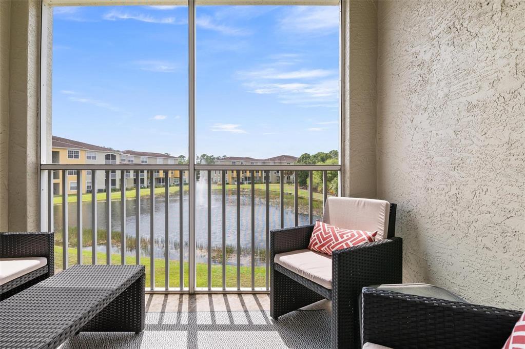 A screened-in balcony features wicker furniture overlooking a pond with a fountain and apartment buildings — 5681 BENTGRASS DRIVE UNIT 204, SARASOTA, FL