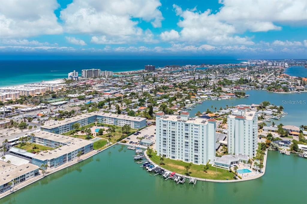 An aerial view shows waterfront high-rise apartment buildings surrounded by a bay and coastal city — 420 64TH AVENUE UNIT 101, ST PETE BEACH, FL